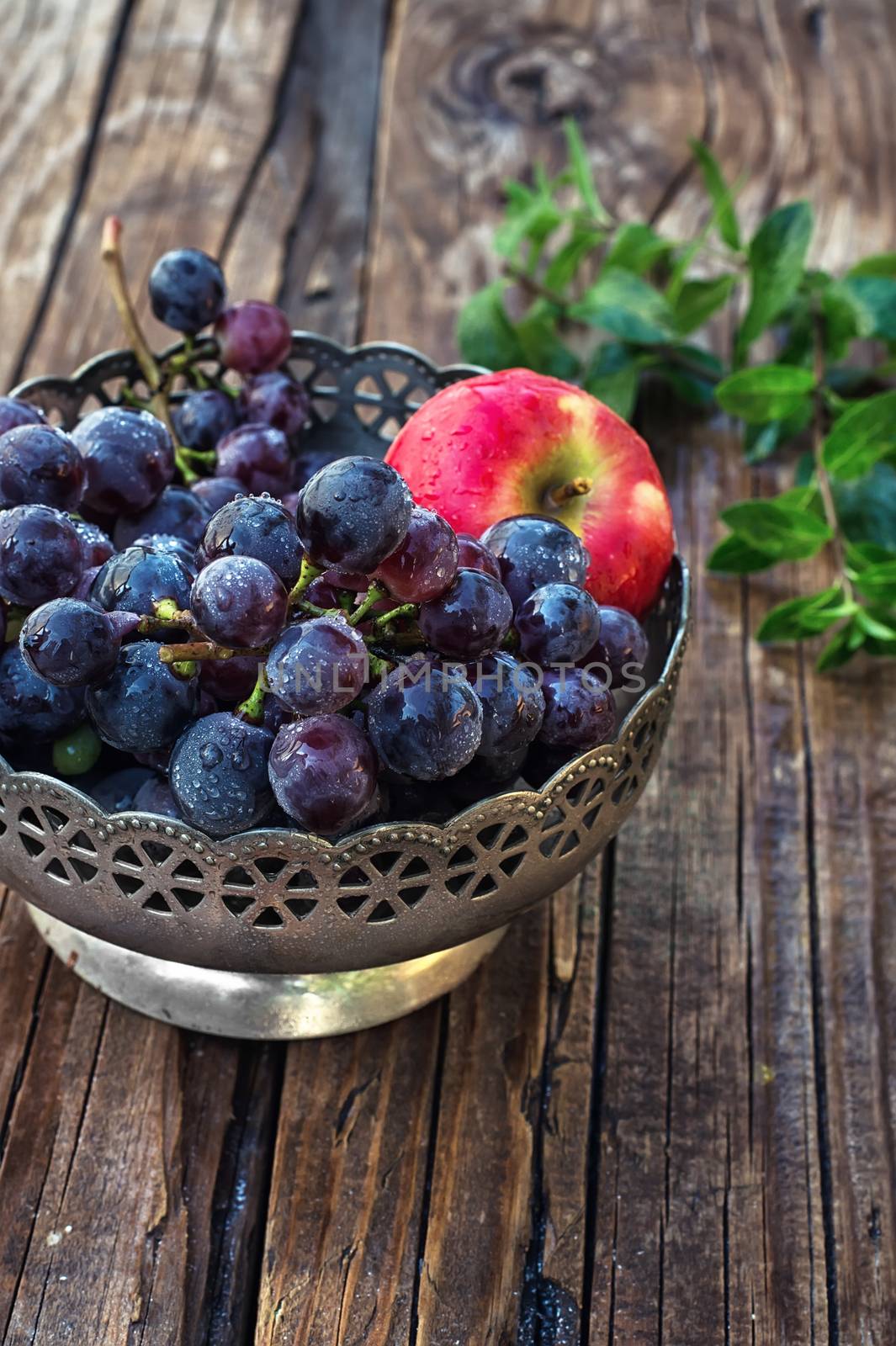 Brush ripe and juicy grapes in  vintage iron vase on wooden background