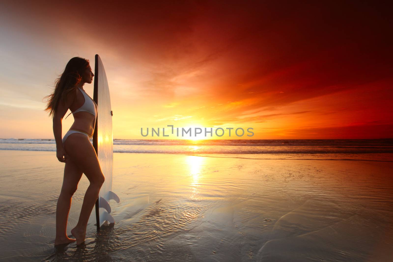 Beautiful surfer girl on the beach at sunset