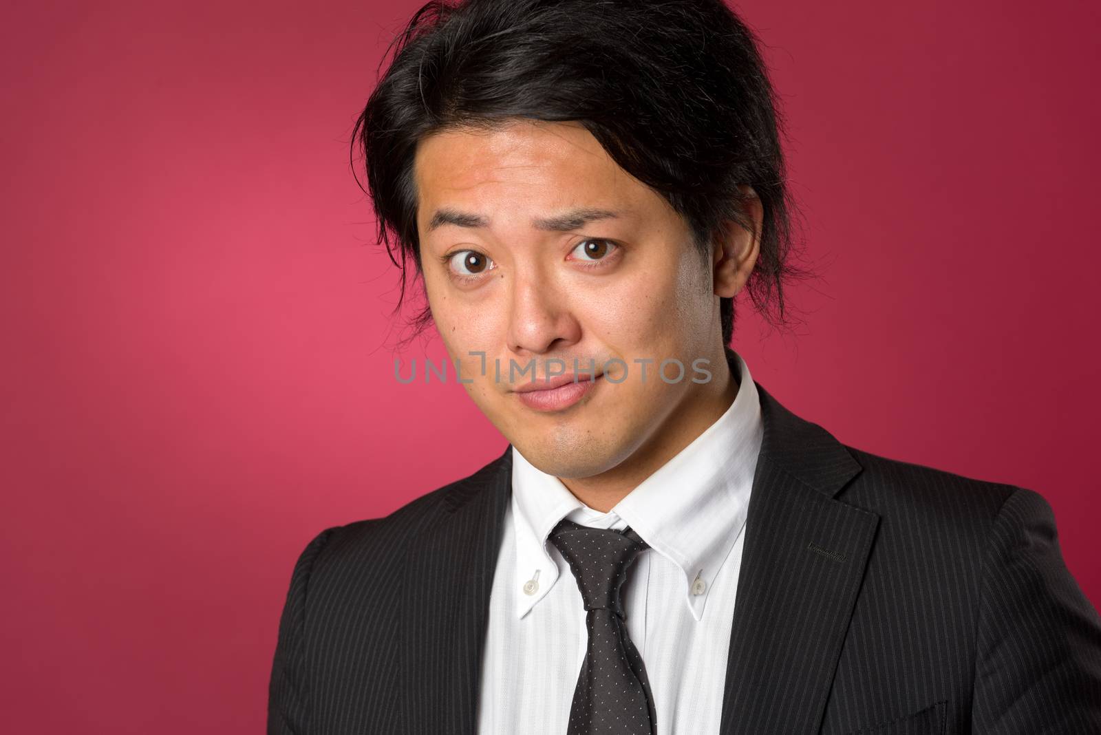 A headshot style portrait of a young Japanese man wearing a business suit on a red background with a slight smile.