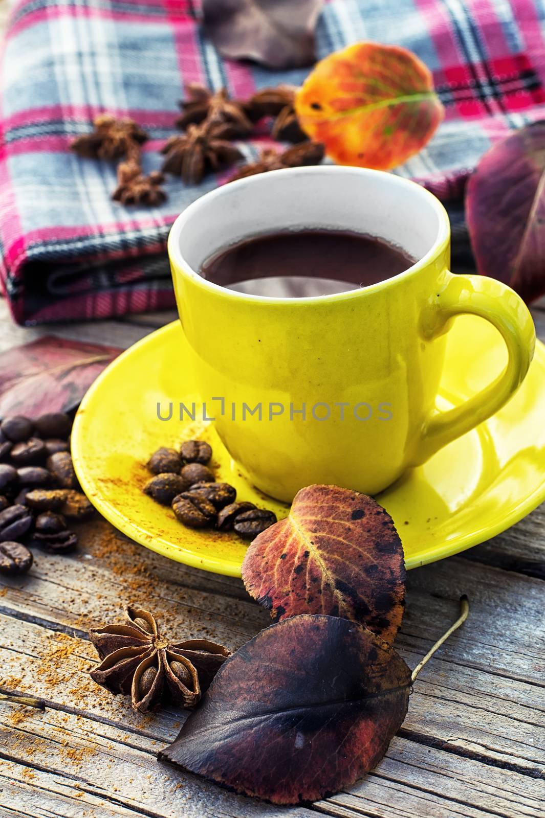 Yellow cup of black coffee on background with warm blanket strewn with autumn leaves