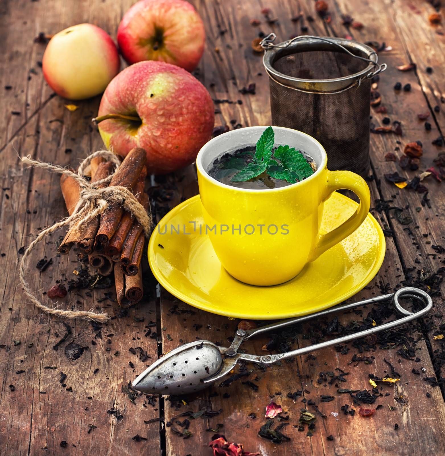 Cup of brewed herbal tea on wooden background strewn with tea leaves