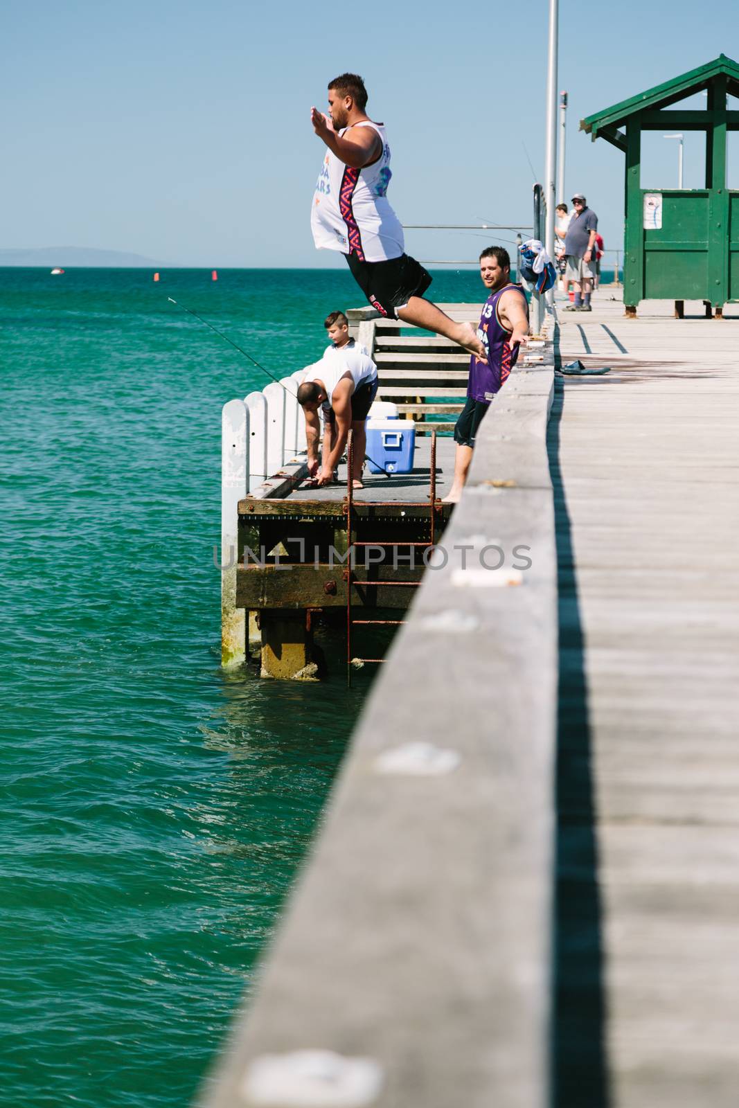 Young men jumping off jetty into water by davidhewison