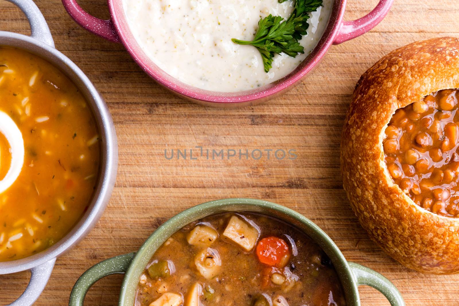 Top view of four partially displayed ceramic and bread bowls full of freshly cooked soup and delicious garnish placed on wooden table