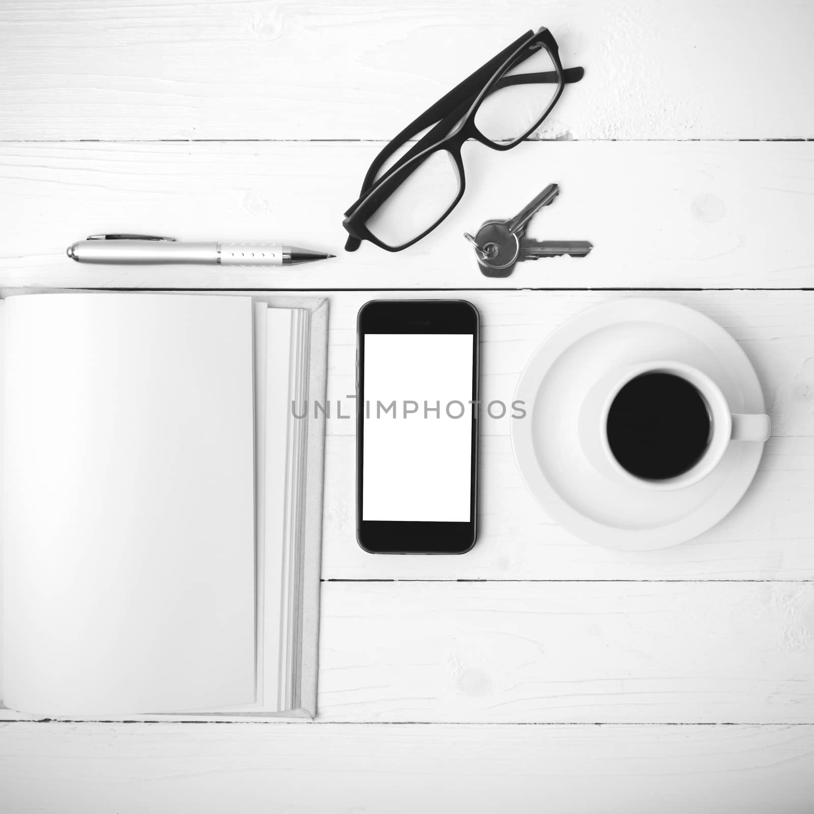 coffee cup with phone, key,eyeglasses and open notebook on white wood table black and white color
