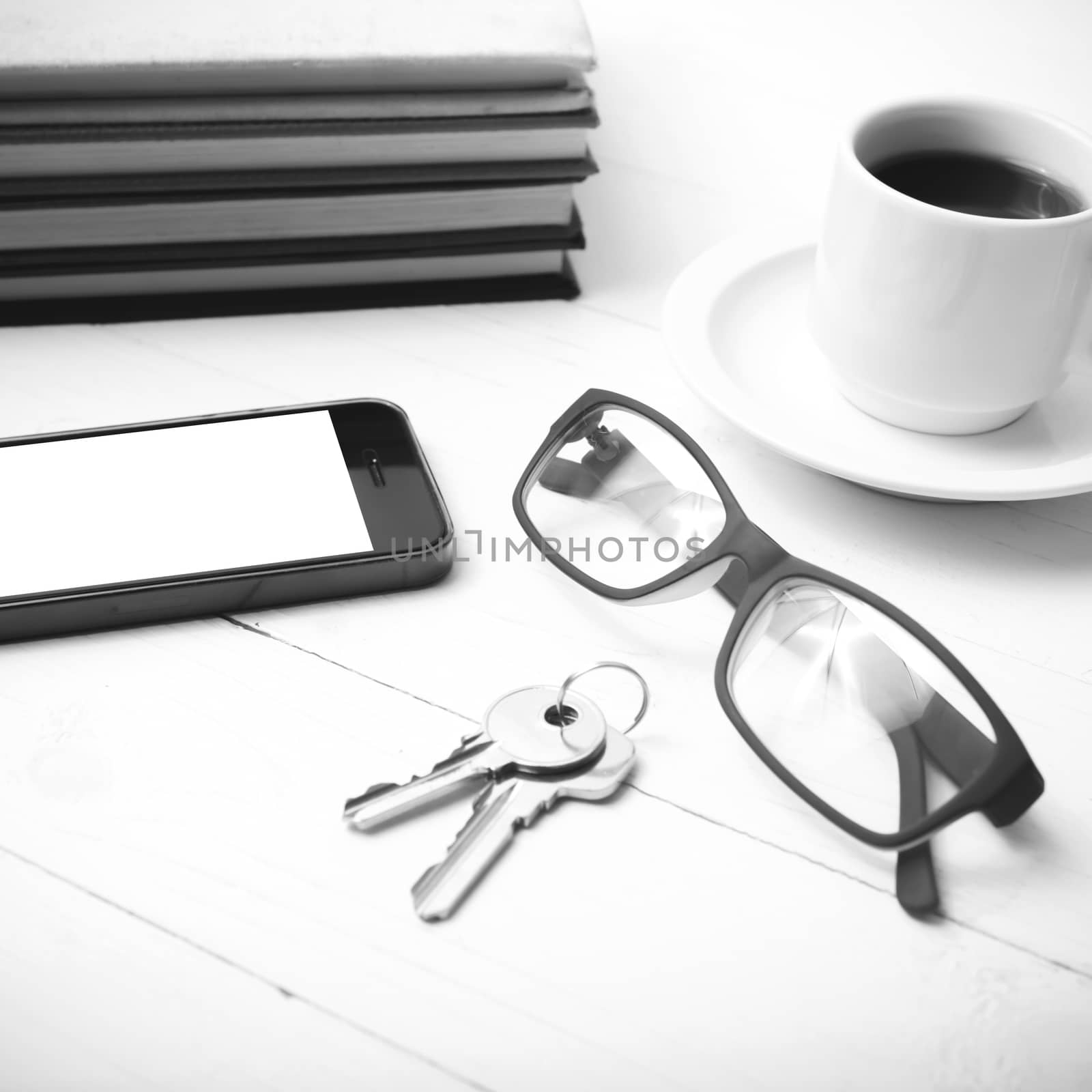 coffee cup with phone,key,eyeglasses and stack of book on white wood table black and white color