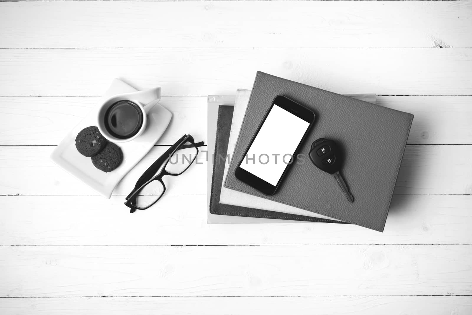 coffe cup with cookie,phone,car key,eyeglasses and stack of book on white wood table black and white color