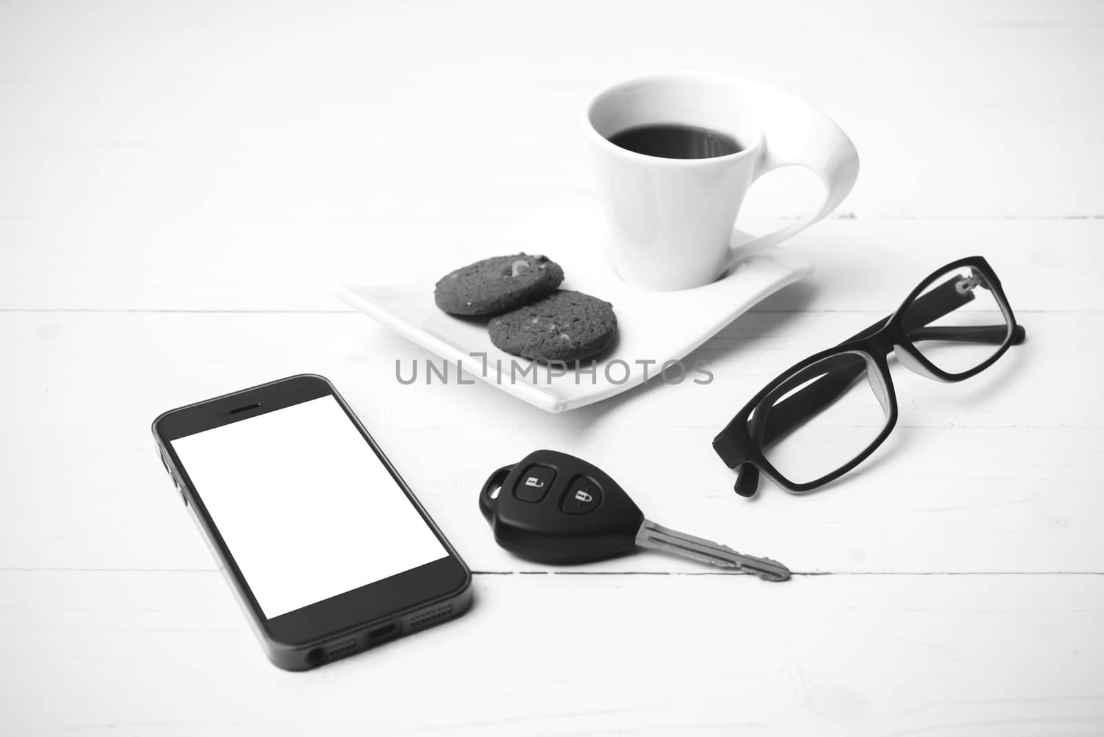 coffee cup with cookie,phone,eyeglasses and car key on white wood table black and white color