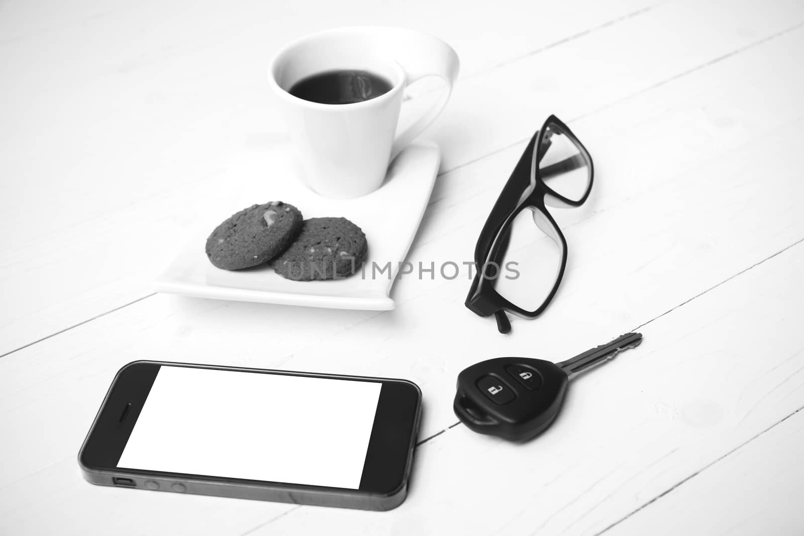 coffee cup with cookie,phone,eyeglasses and car key on white wood table black and white color
