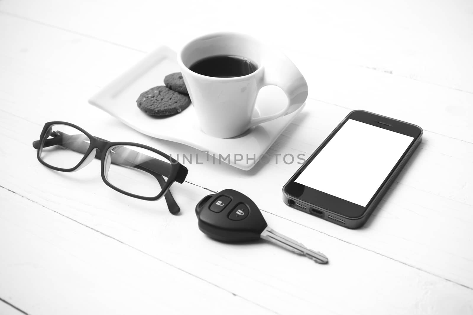 coffee cup with cookie,phone,eyeglasses and car key on white wood table black and white color