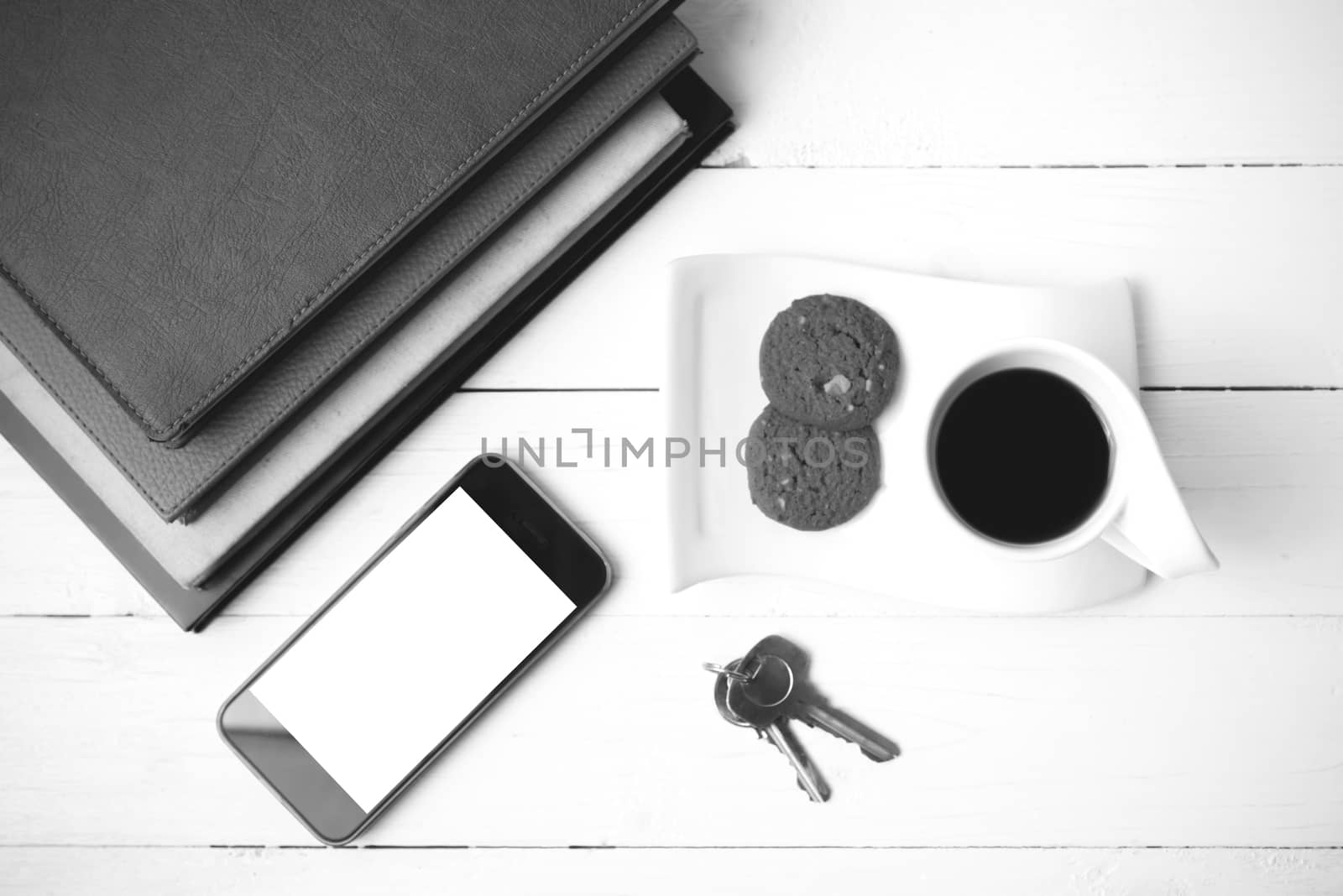 coffee cup with cookie,phone,stack of book and key on white wood table black and white color