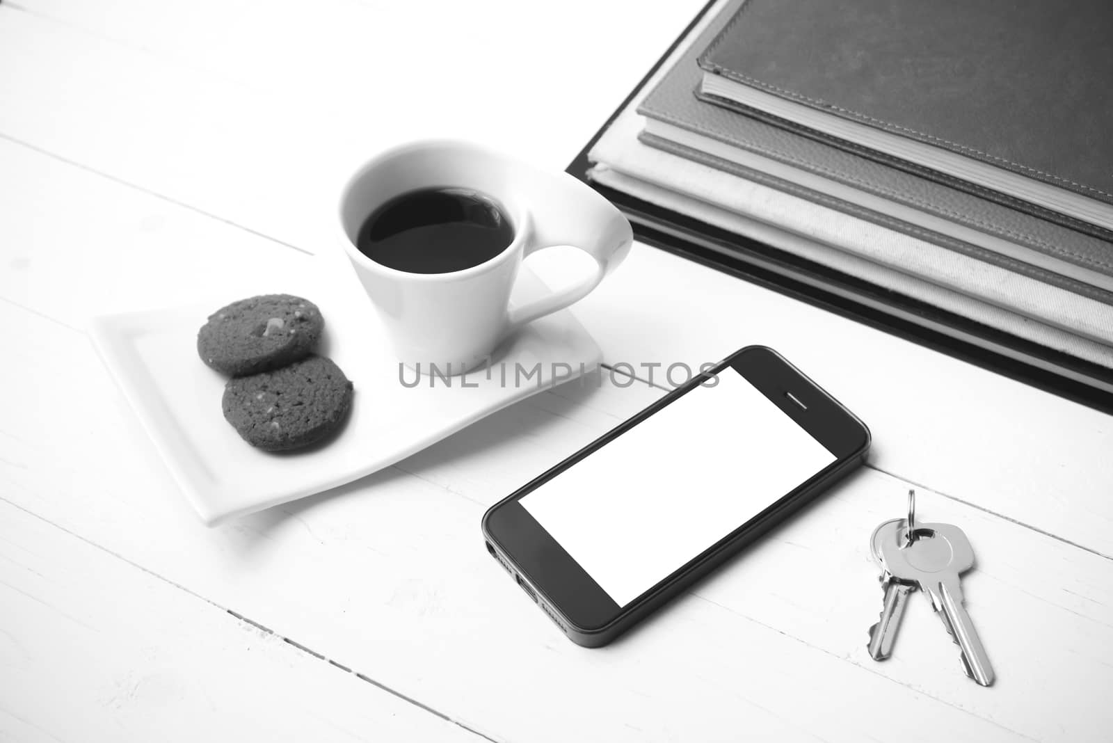 coffee cup with cookie,phone,stack of book and key on white wood table black and white color