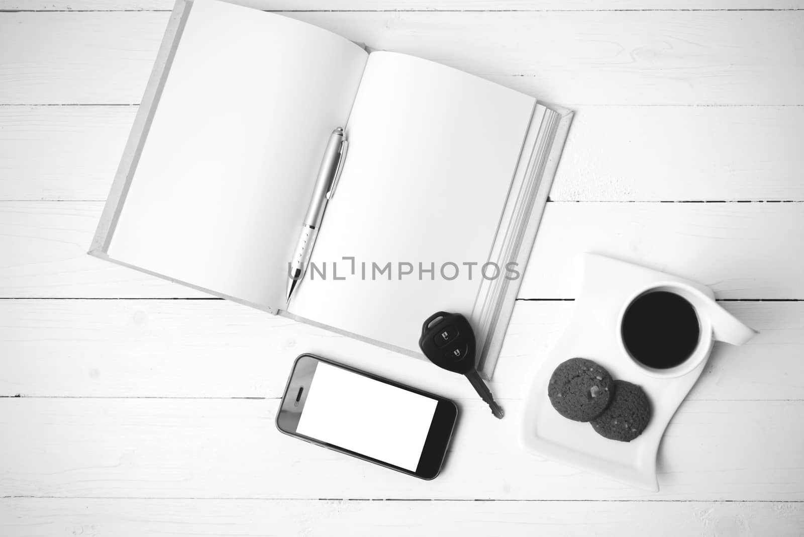 coffee cup with cookie,phone,open notebook and car key on white wood table black and white color