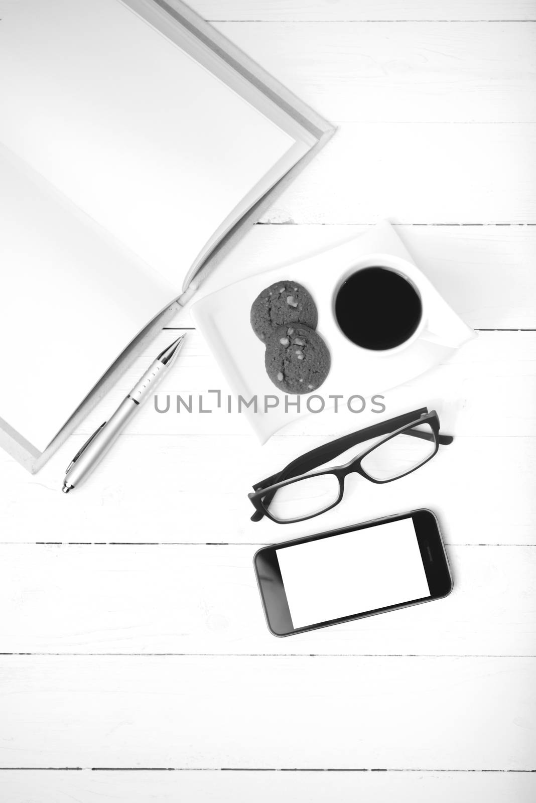 coffee cup with cookie,phone,notebook and eyeglasses on white wood table black and white color