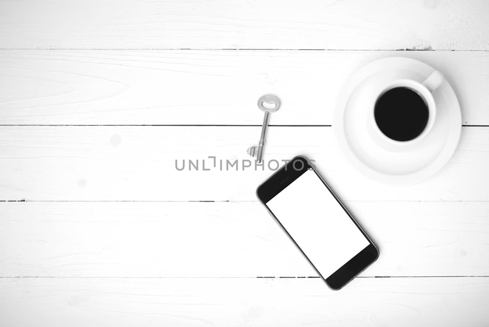 coffee cup with phone and key on white wood table black and white color