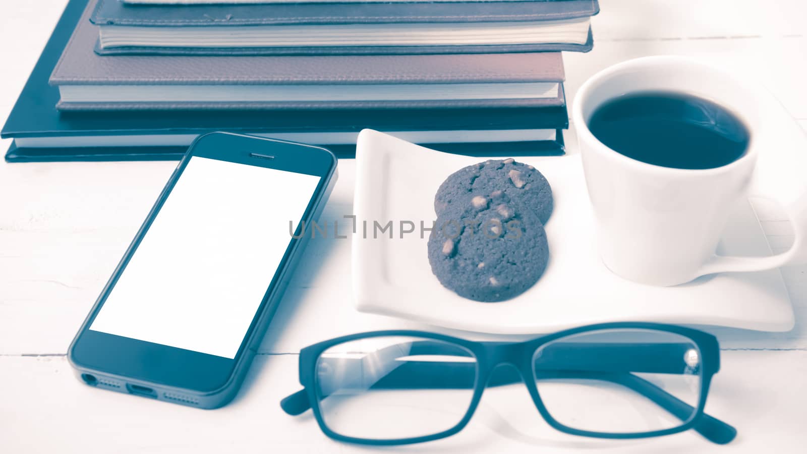 coffee cup with cookie,phone,stack of book and eyeglasses on white wood table vintage style