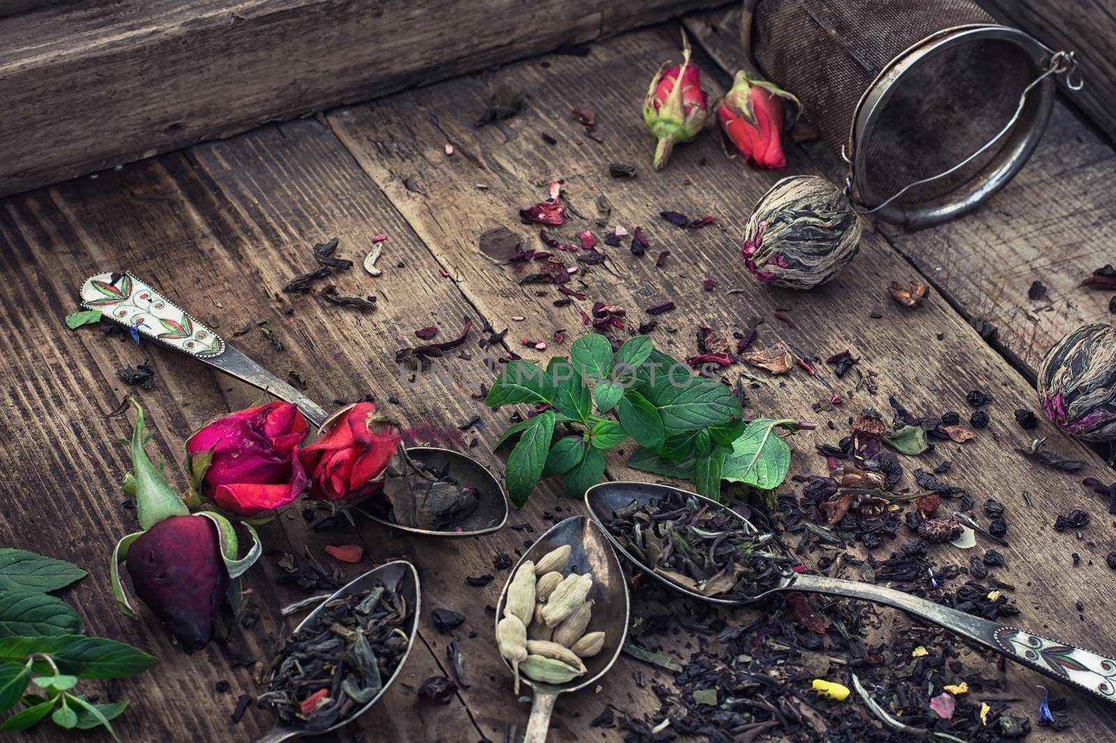 Vintage spoons with different varieties of tea on vintage wooden plank background.