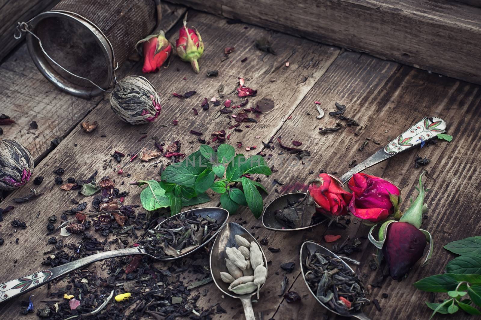 Vintage spoons with different varieties of tea on vintage wooden plank background.