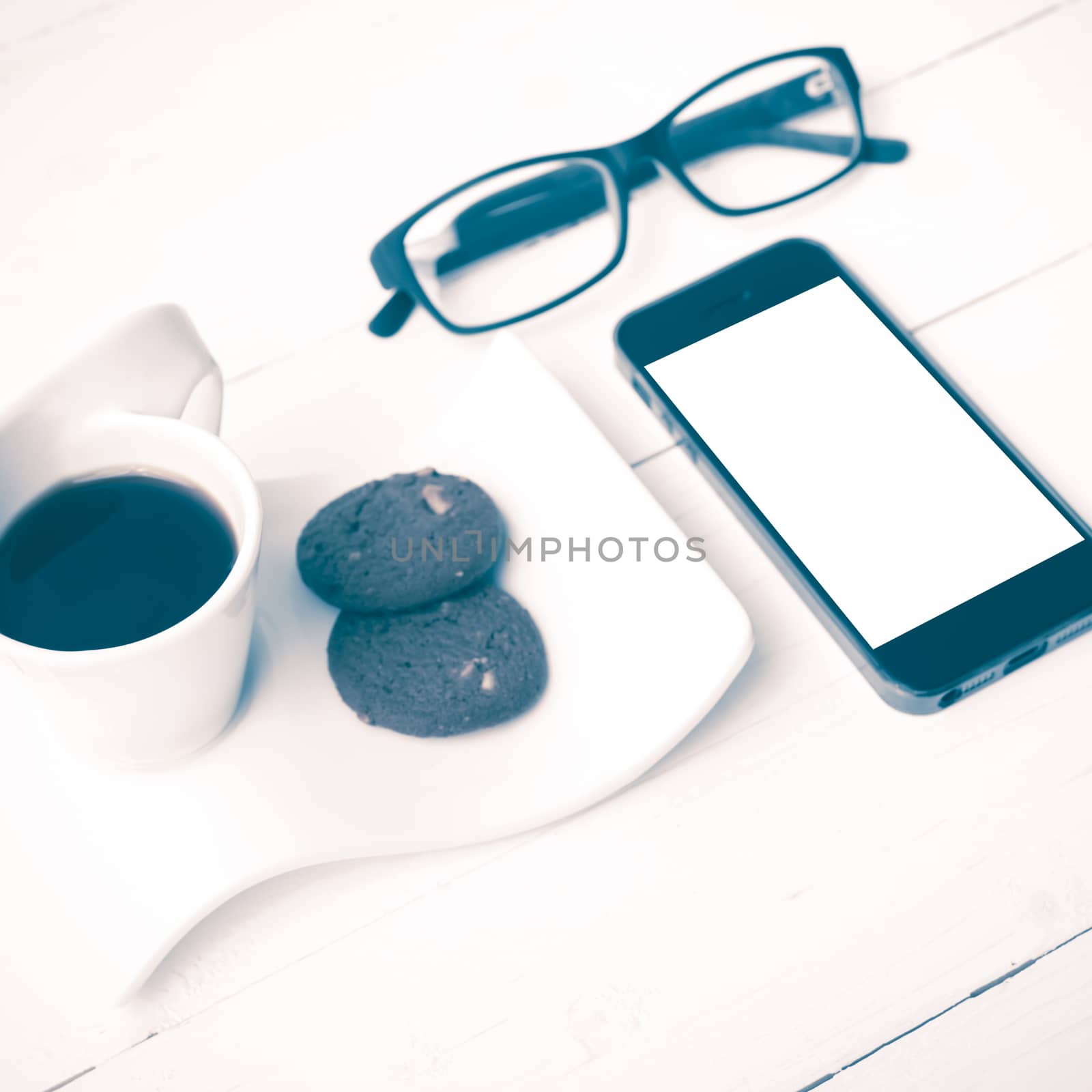 coffee cup with cookie,phone and eyeglasses on white wood table vintage style
