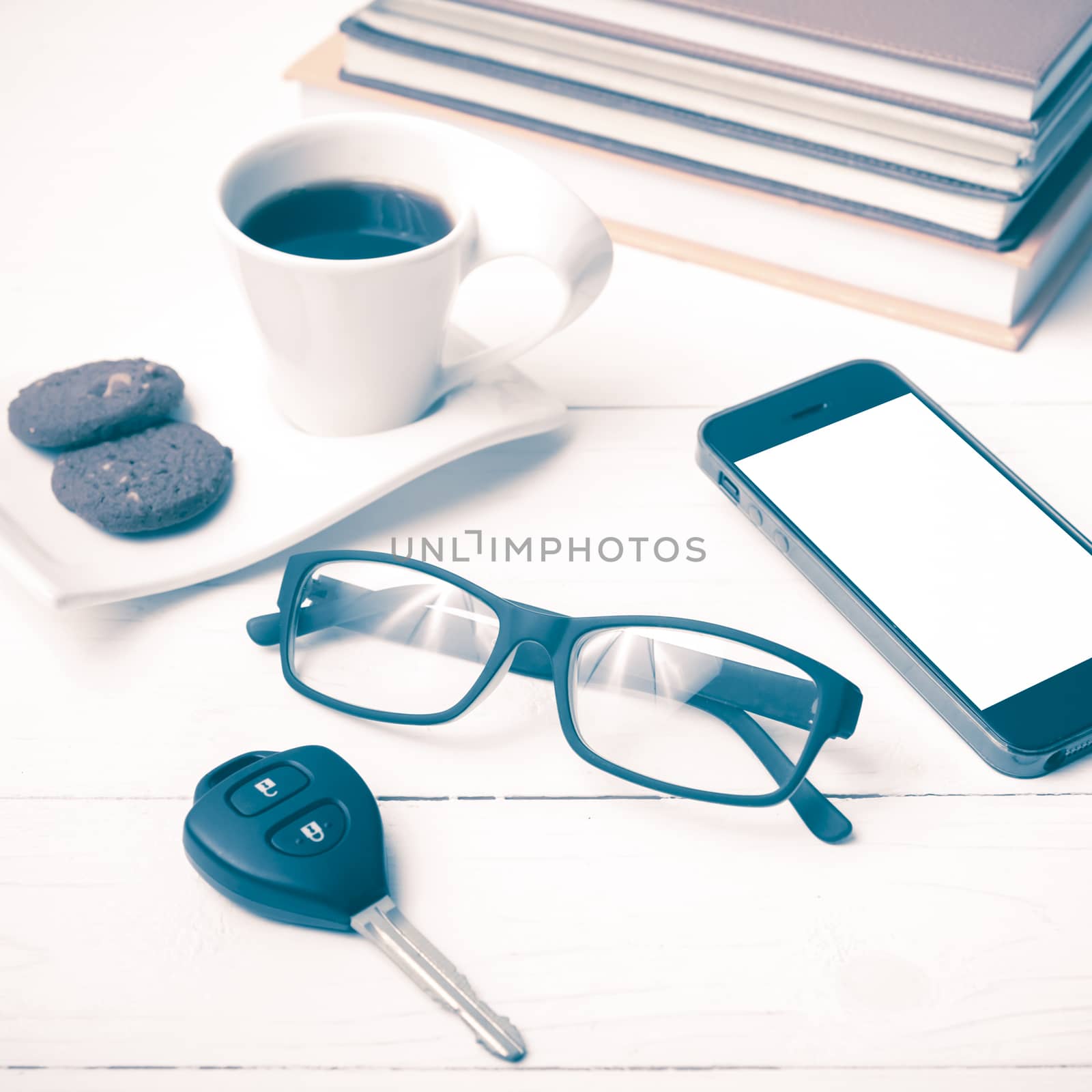 coffe cup with cookie,phone,car key,eyeglasses and stack of book on white wood table vintage style