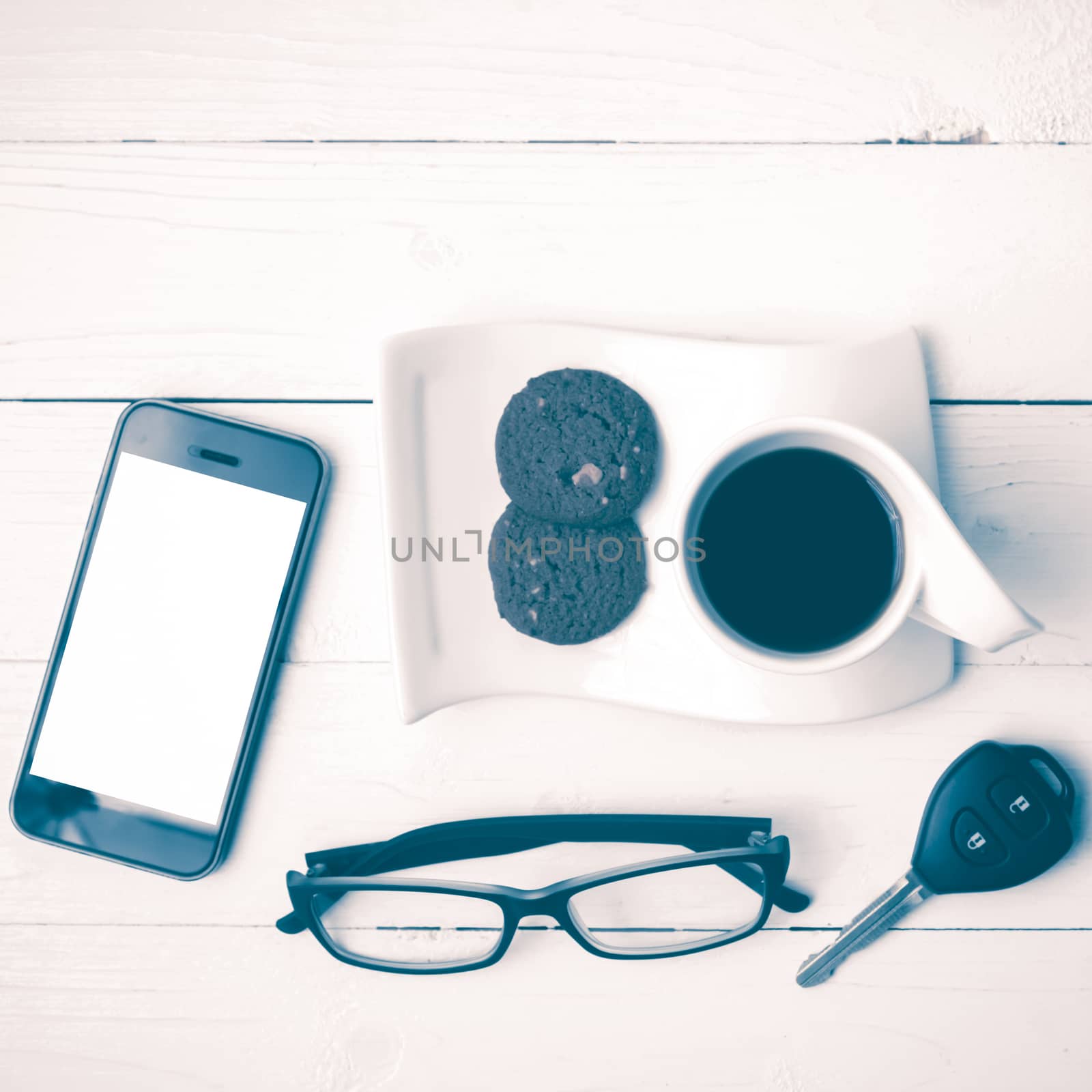 coffee cup with cookie,phone,eyeglasses and car key on white wood table vintage style