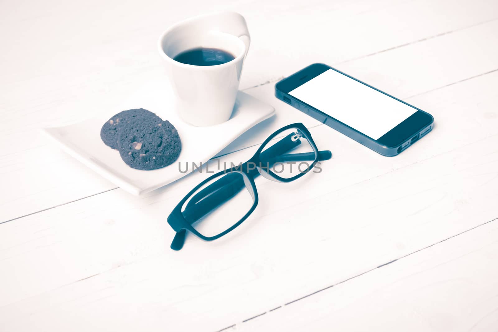 coffee cup with cookie,phone and eyeglasses on white wood table vintage style