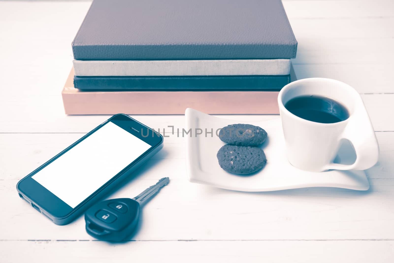 coffe cup with cookie,phone,car key and stack of book on white wood table vintage style