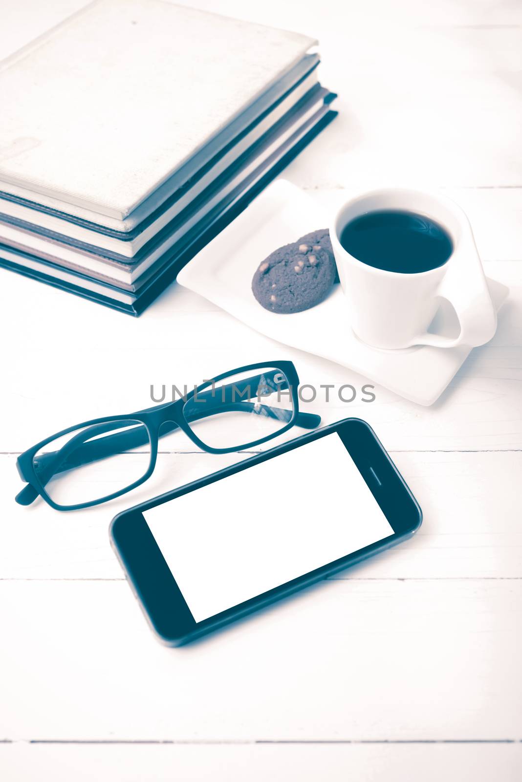 coffee cup with cookie,phone,stack of book and eyeglasses on white wood table vintage style