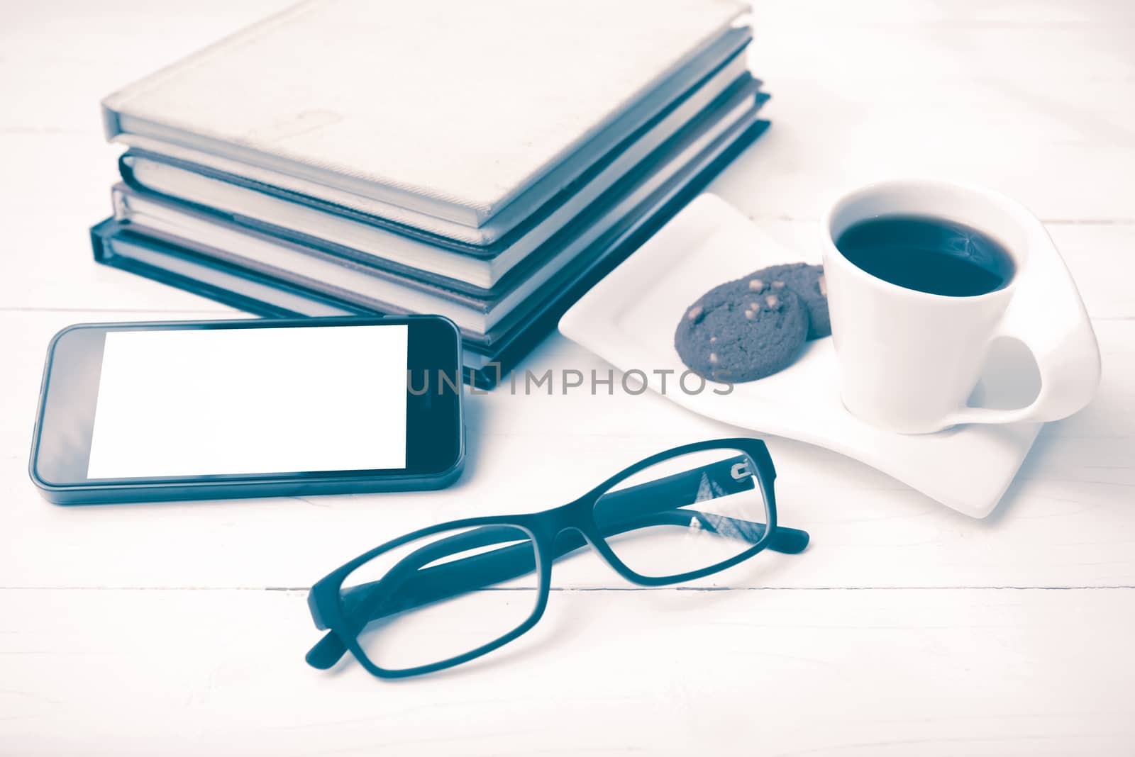 coffee cup with cookie,phone,stack of book and eyeglasses on white wood table vintage style