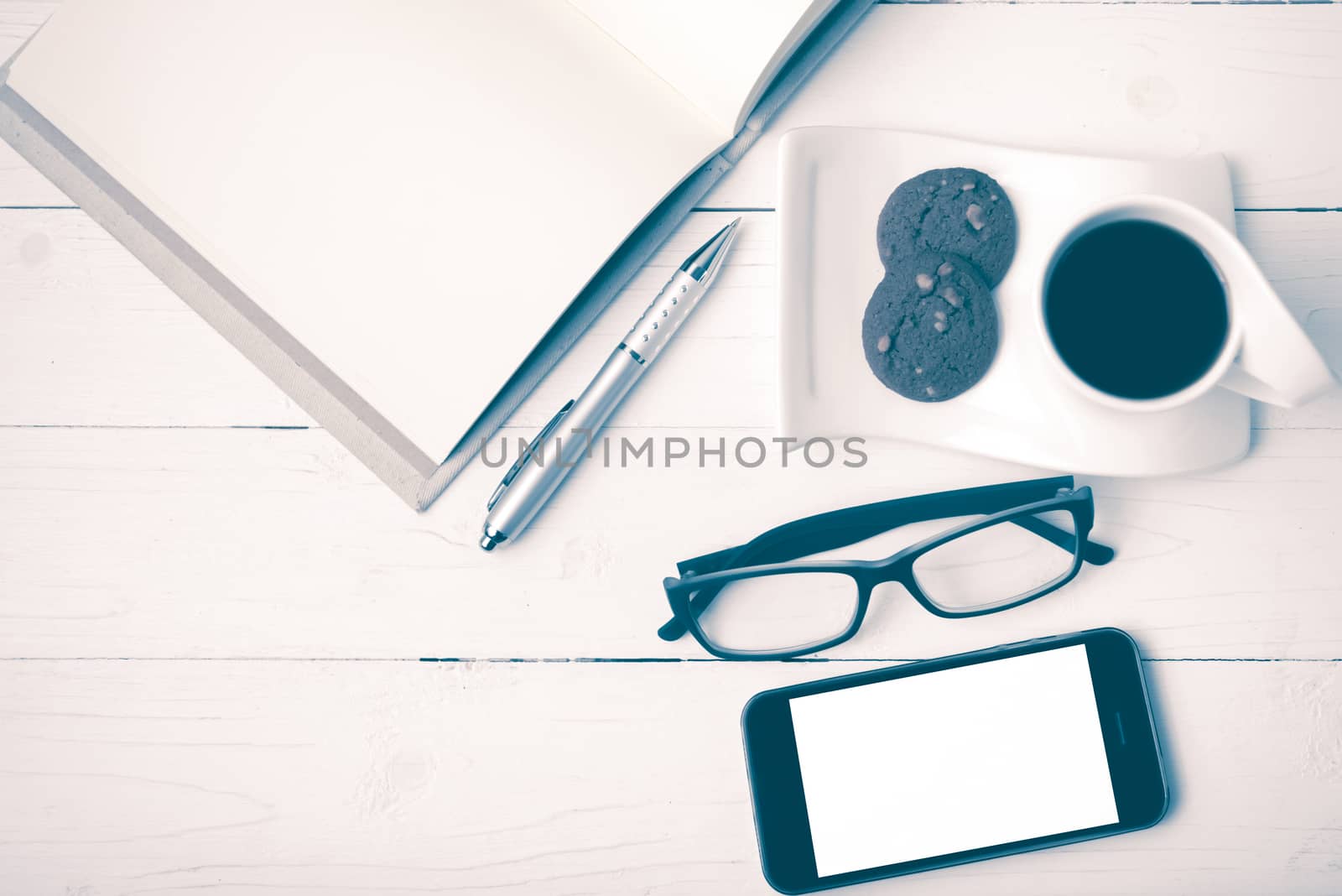 coffee cup with cookie,phone,notebook and eyeglasses on white wood table vintage style