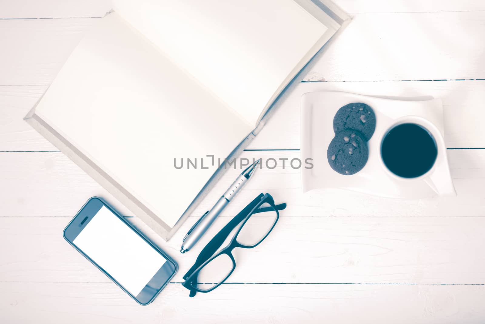 coffee cup with cookie,phone,notebook and eyeglasses on white wood table vintage style