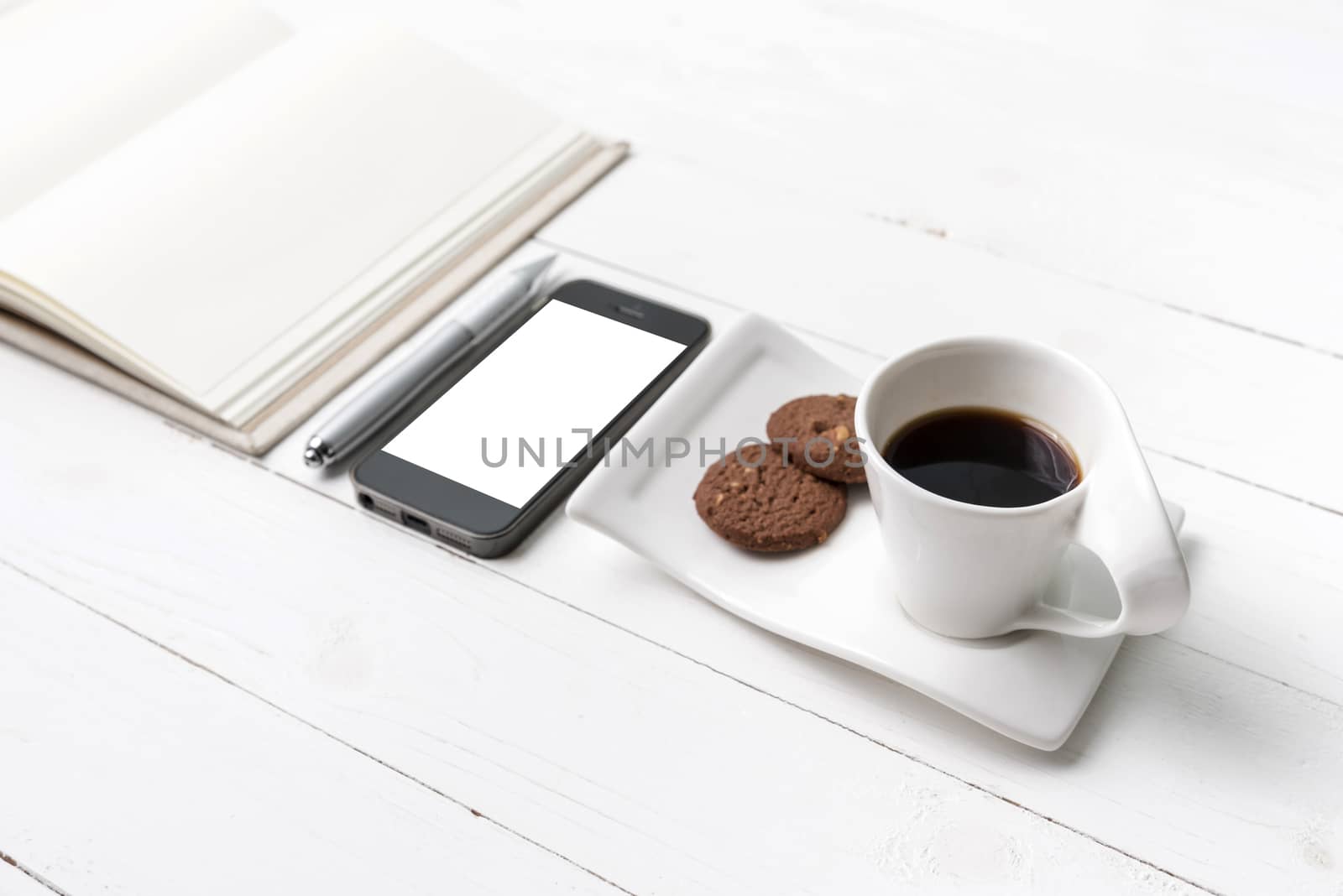 coffee cup with cookie,phone with notebook and pen on white wood table