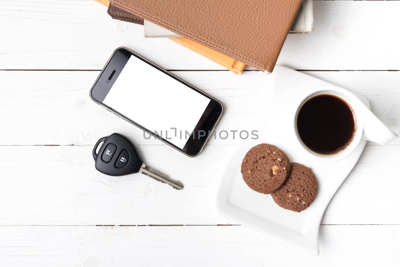 coffe cup with cookie,phone,car key and stack of book on white wood table