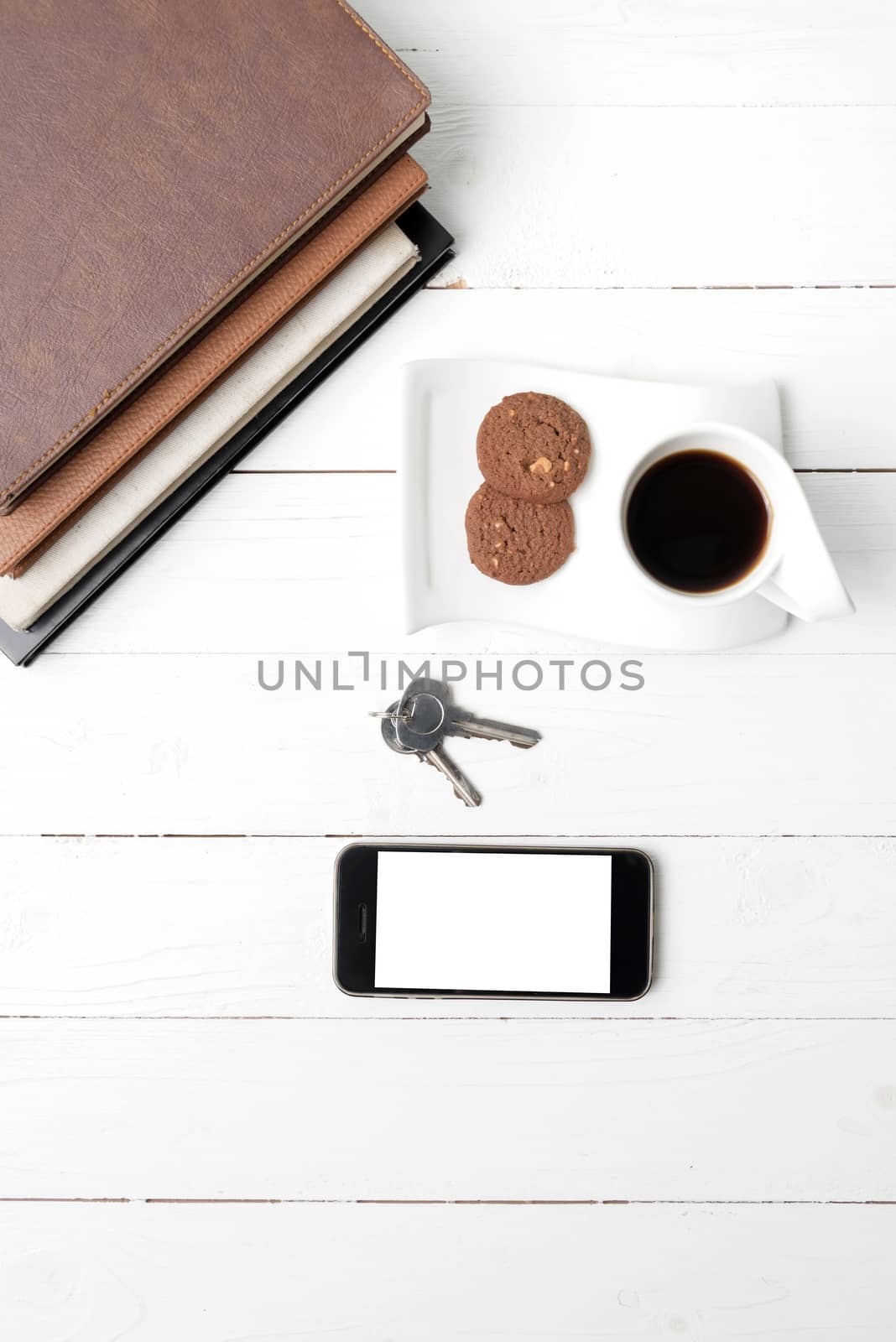 coffee cup with cookie,phone,stack of book and key on white wood table