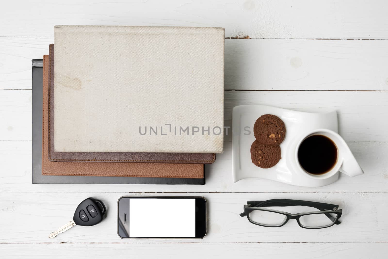 coffee cup with cookie,phone,stack of book and car key on white wood table