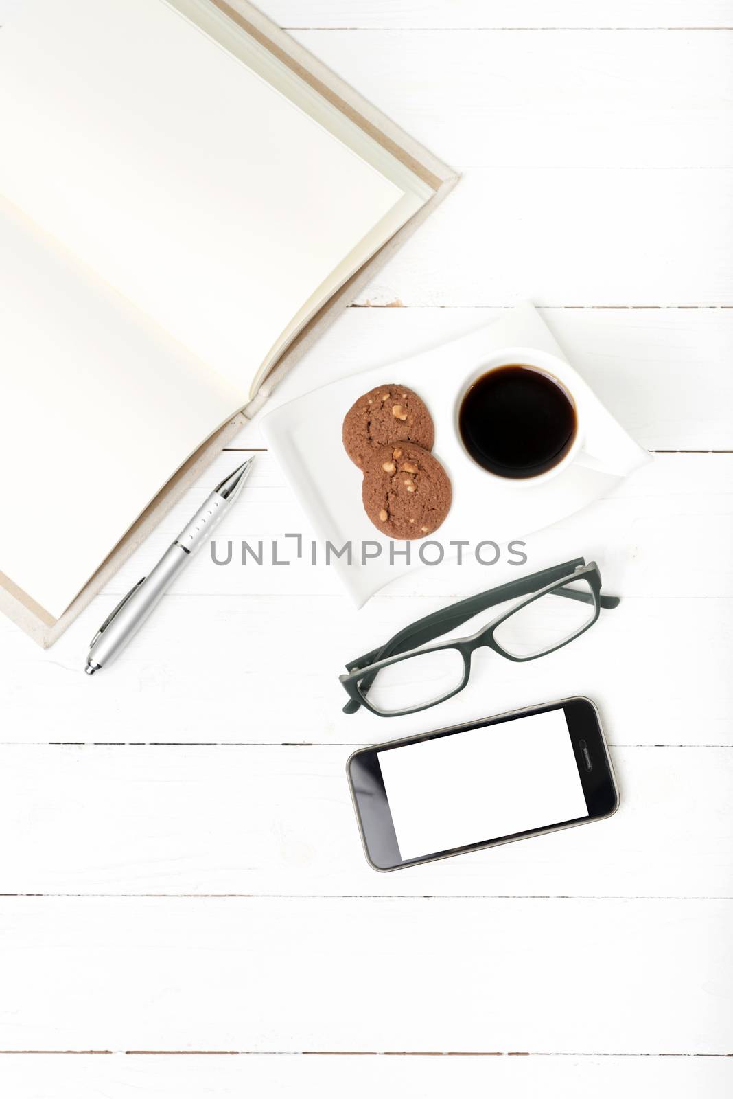 coffee cup with cookie,phone,notebook and eyeglasses on white wood table