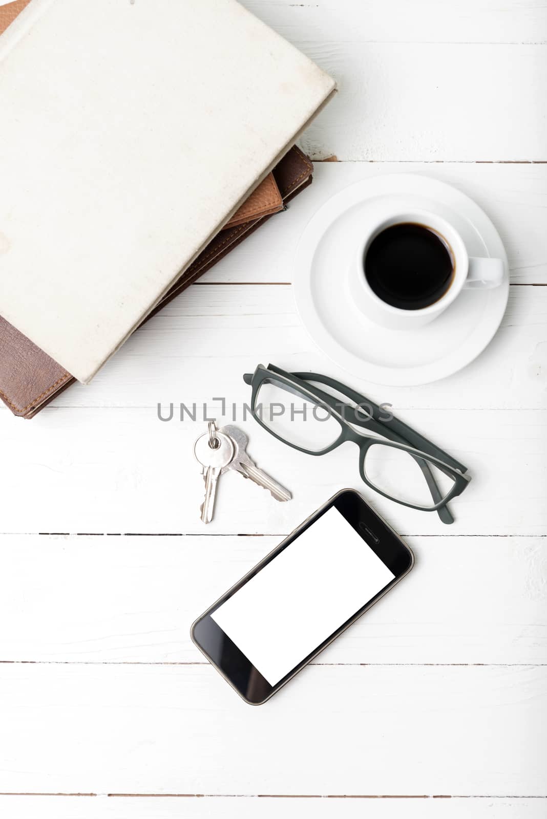 coffee cup with phone,key,eyeglasses and stack of book on white wood table