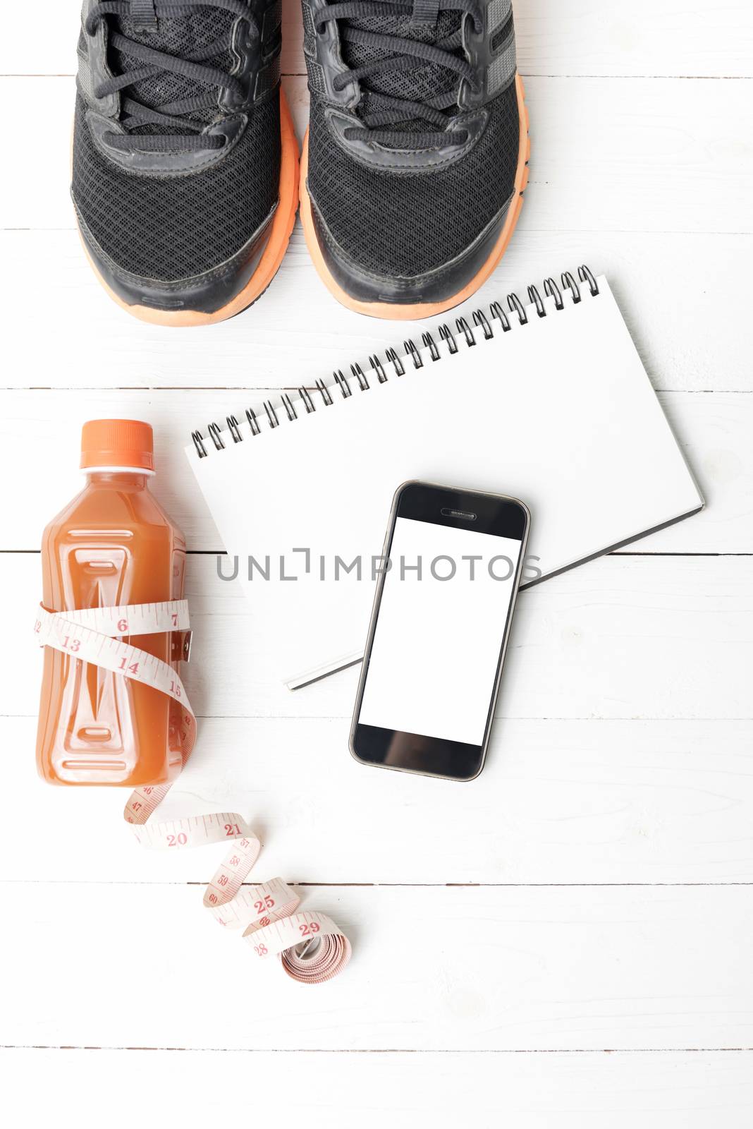 fitness equipment:running shoes,juice,measuring tape,notepad and phone on white wood background