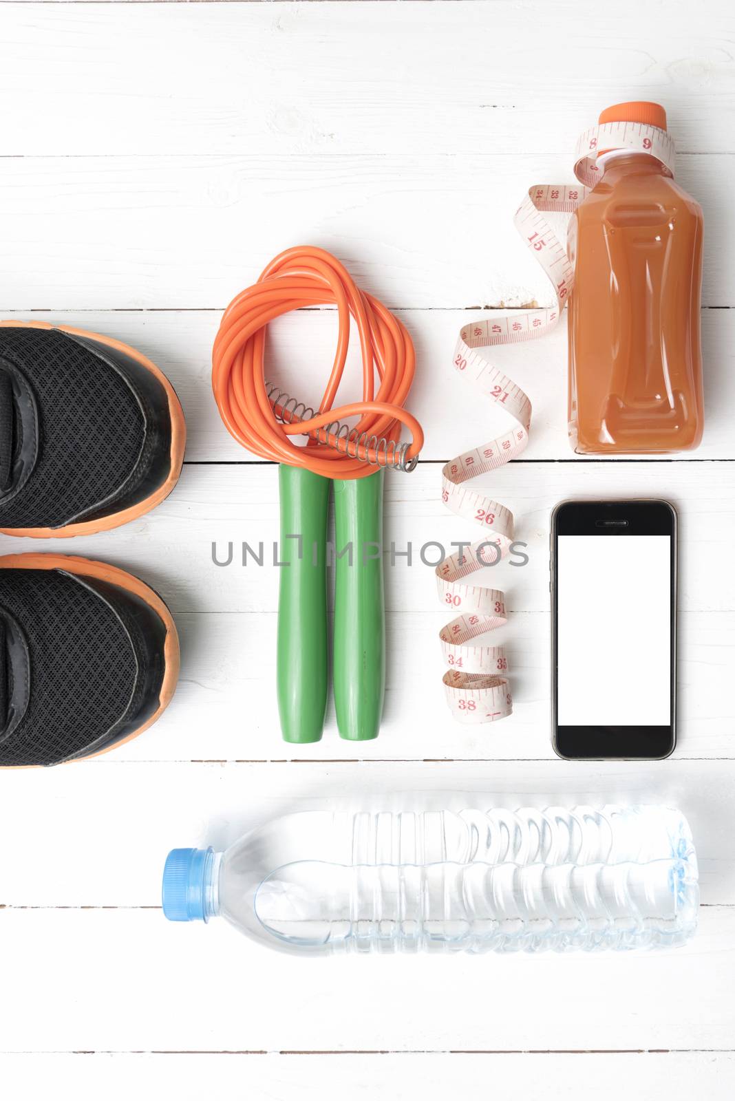 fitness equipment:running shoes,phone,measuring tape,water,juice and jumpong rope on white wood background
