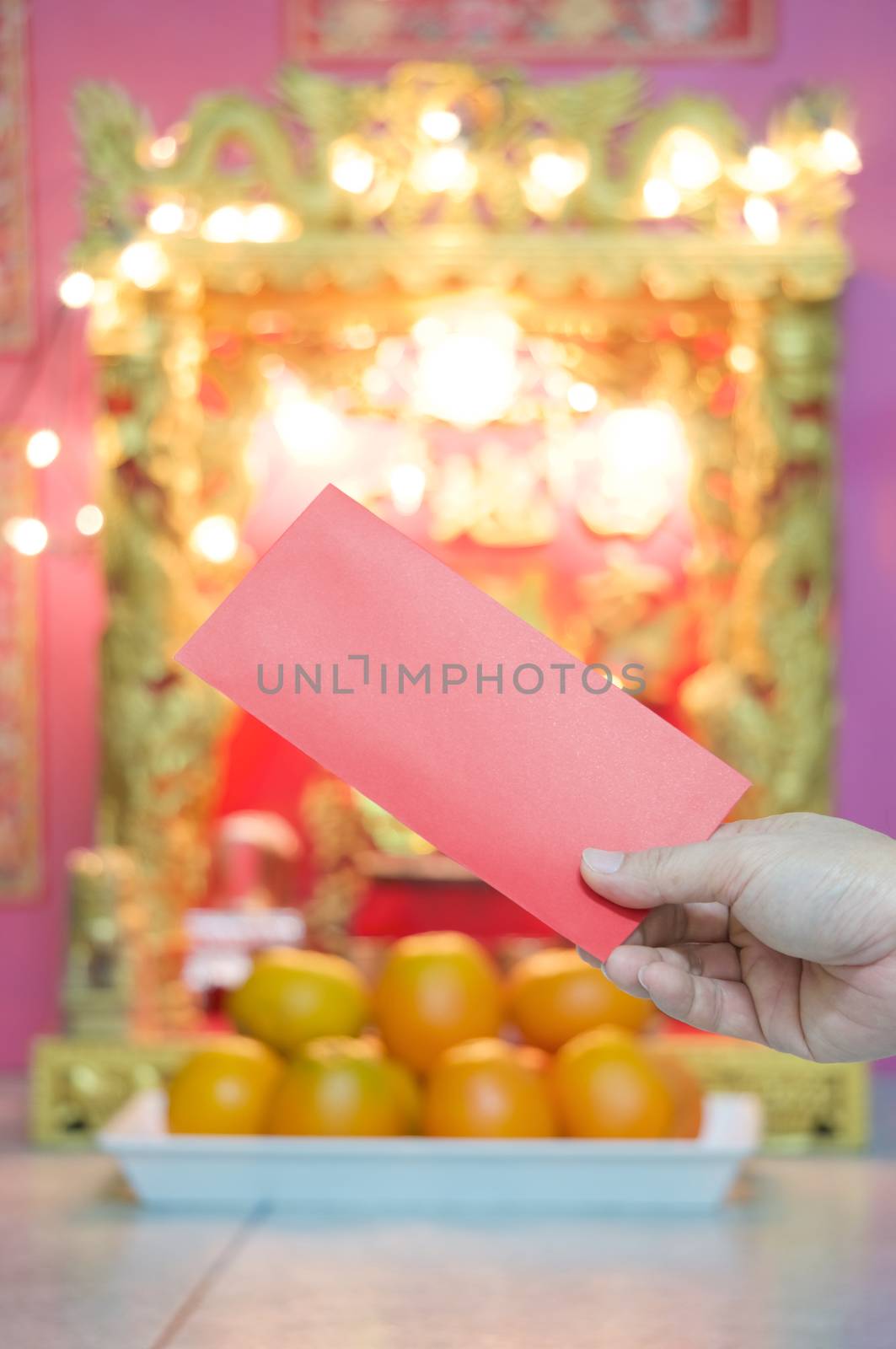 Hand of man holding red envelope in chinese new year festival have blur Chinese shrine housing a statue as background.