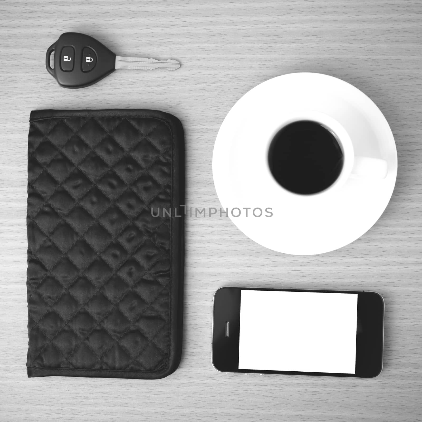 coffee cup with phone car key and wallet on wood background black and white color