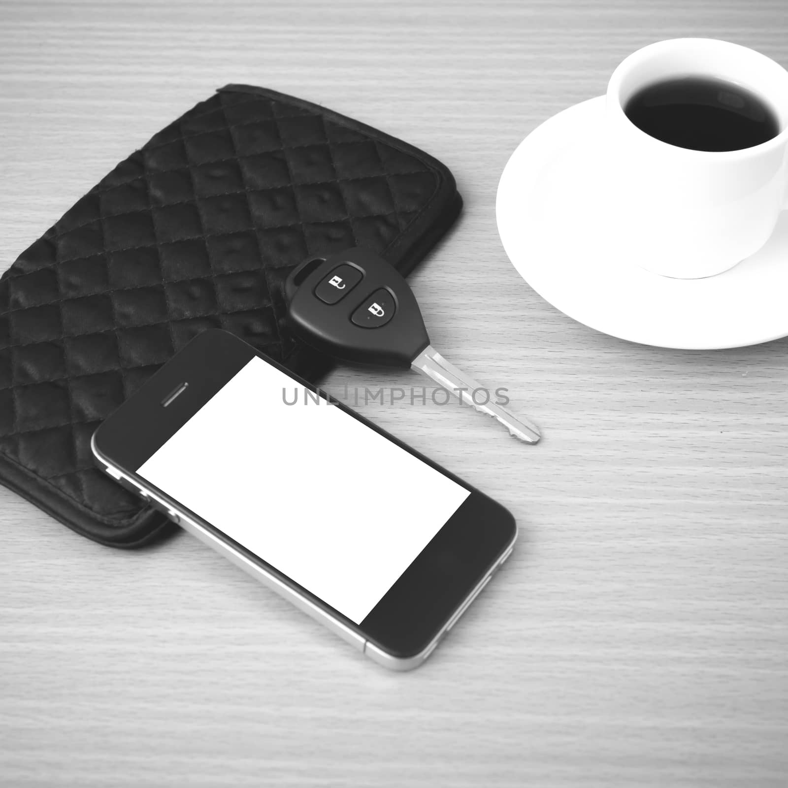 coffee cup with phone car key and wallet on wood background black and white color