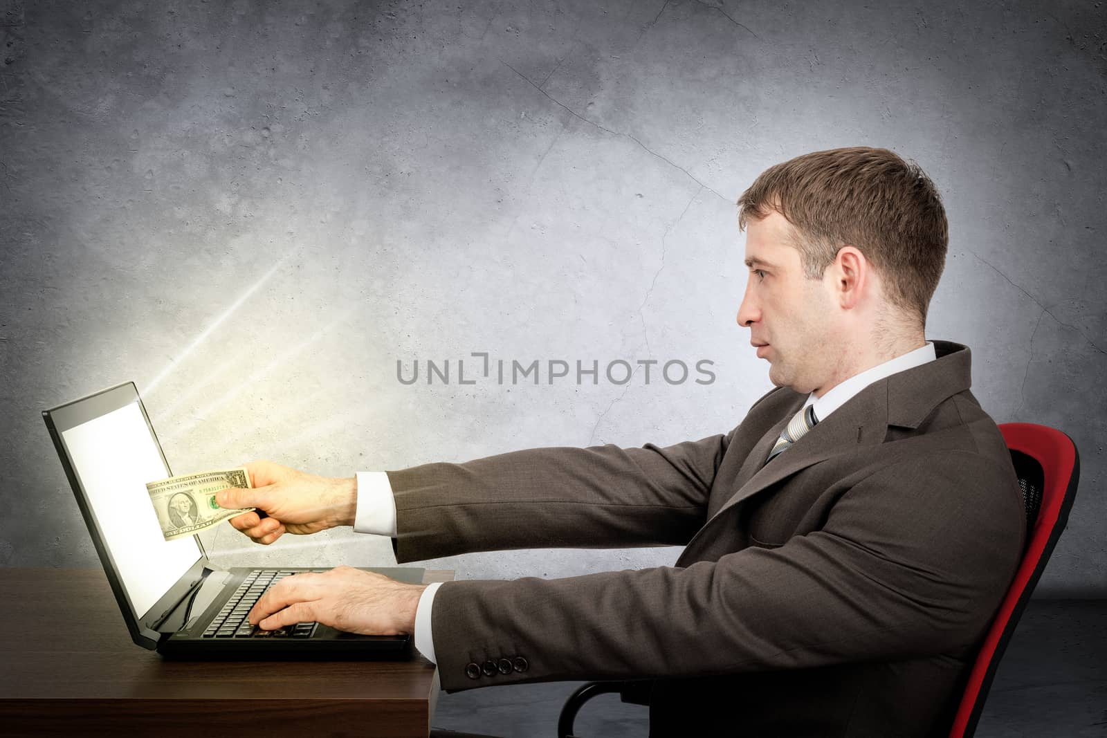 Businessman giving dollar to laptop on grey wall background