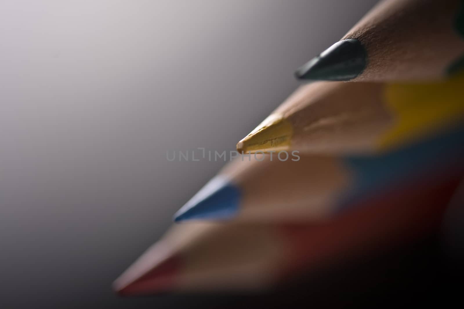 Group of four colored pencils with shallow depth of field on grey background. 