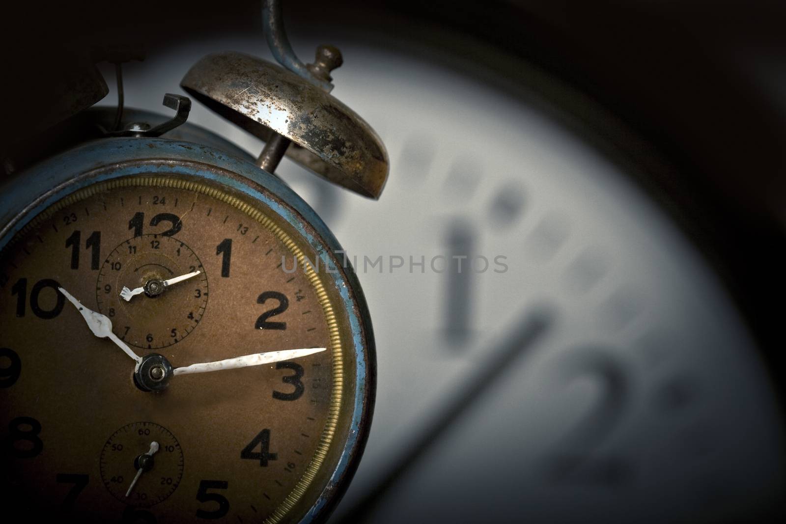 Old rusted alarm clock with another larger clock face in the background