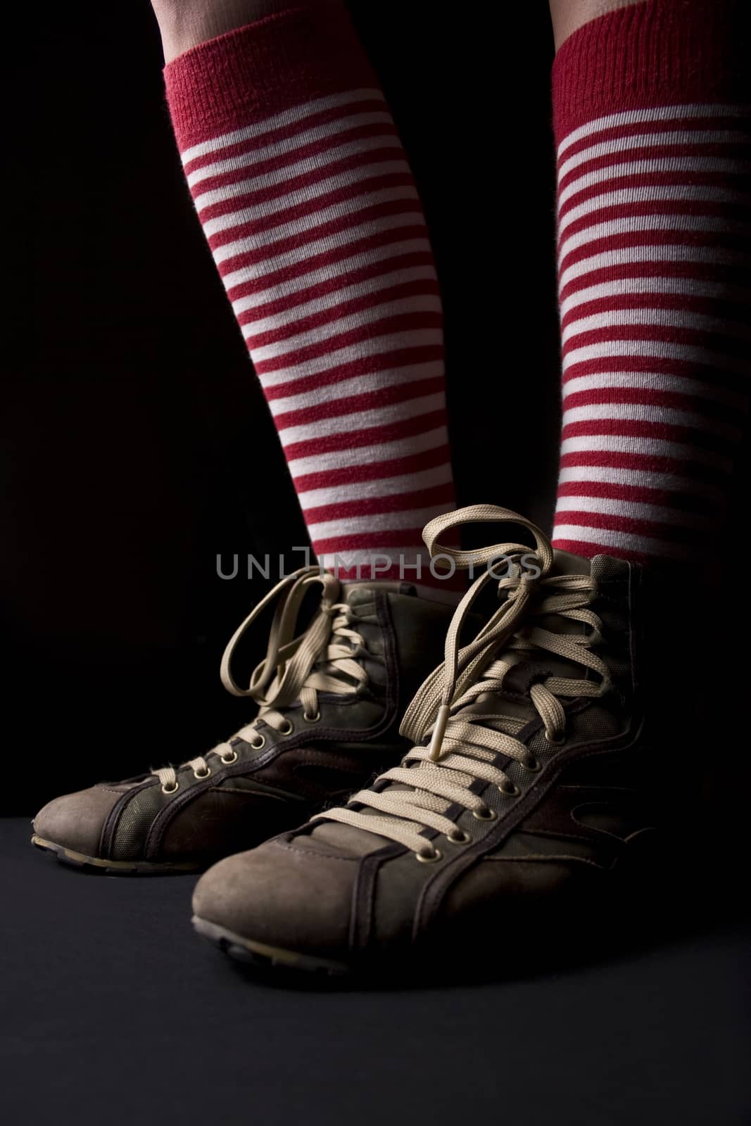 Woman’s legs with sneakers and a pair of red socks with white stripes on dark background