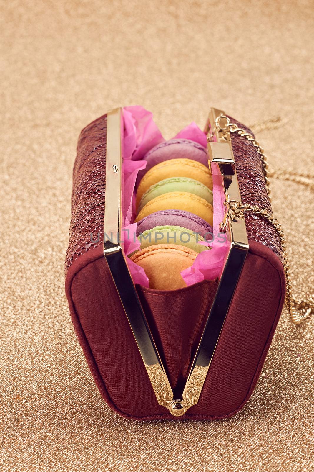 Macarons french in handbag. Luxury shiny glamor fashion clutch. Sweet colorful dessert. Unusual creative art, gold party background, bokeh, closeup. Vintage