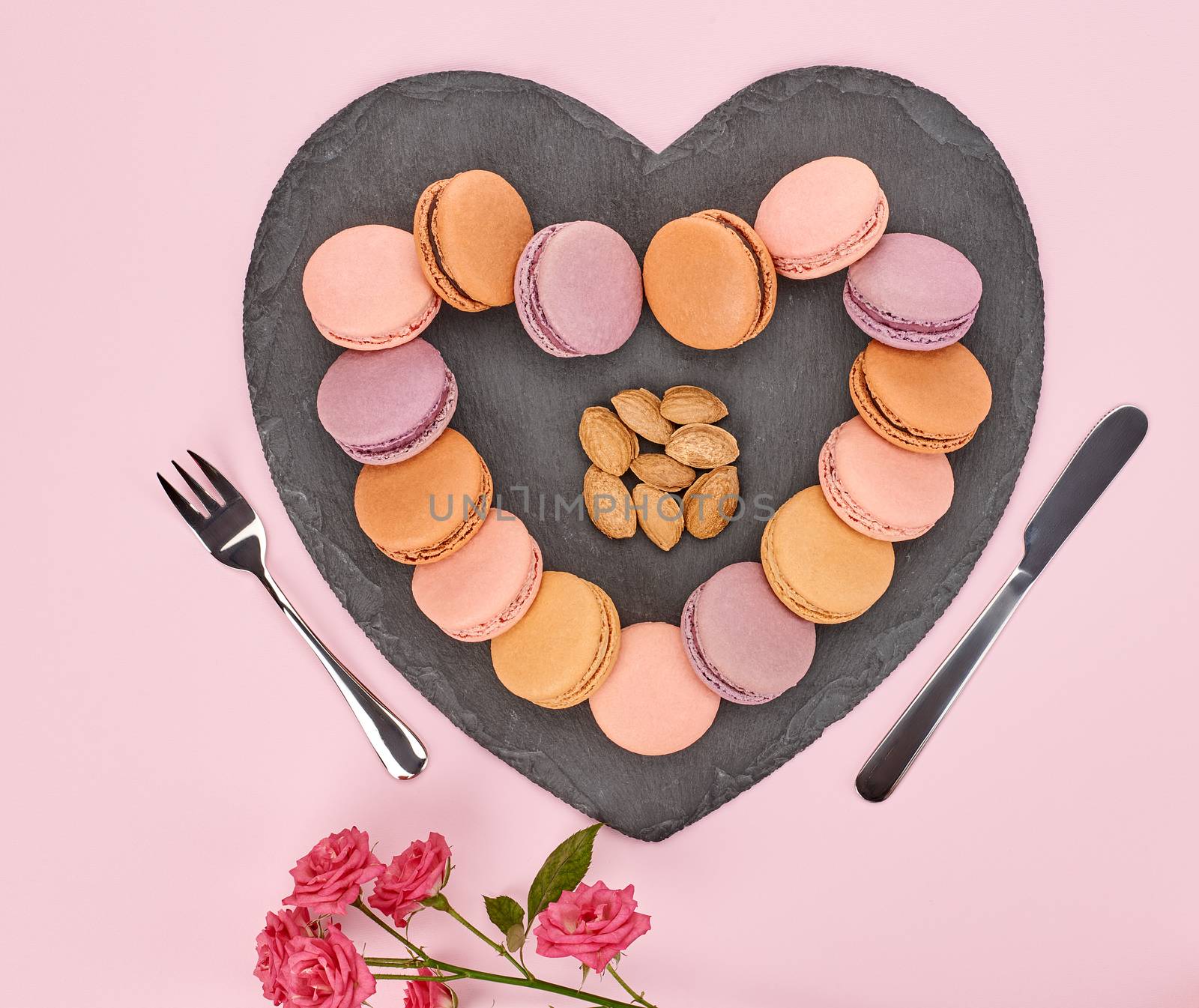 Still life, macarons sweet colorful, heart shape, fork knife. Black placemat, roses almond. French dessert, table setting. Unusual creative romantic, pink background. Concept love story.Valentines Day