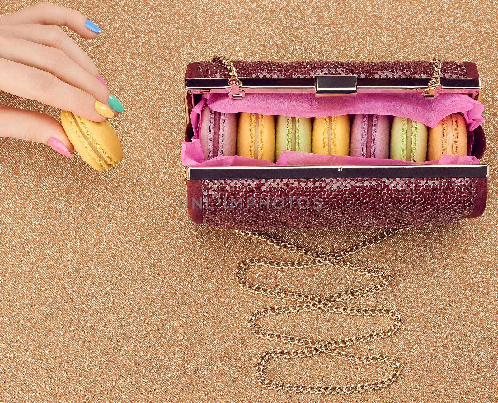 Macarons french in handbag, woman hand. Luxury shiny glamor fashion clutch. Sweet colorful dessert. Unusual creative art, gold party background, bokeh, copyspase. Vintage