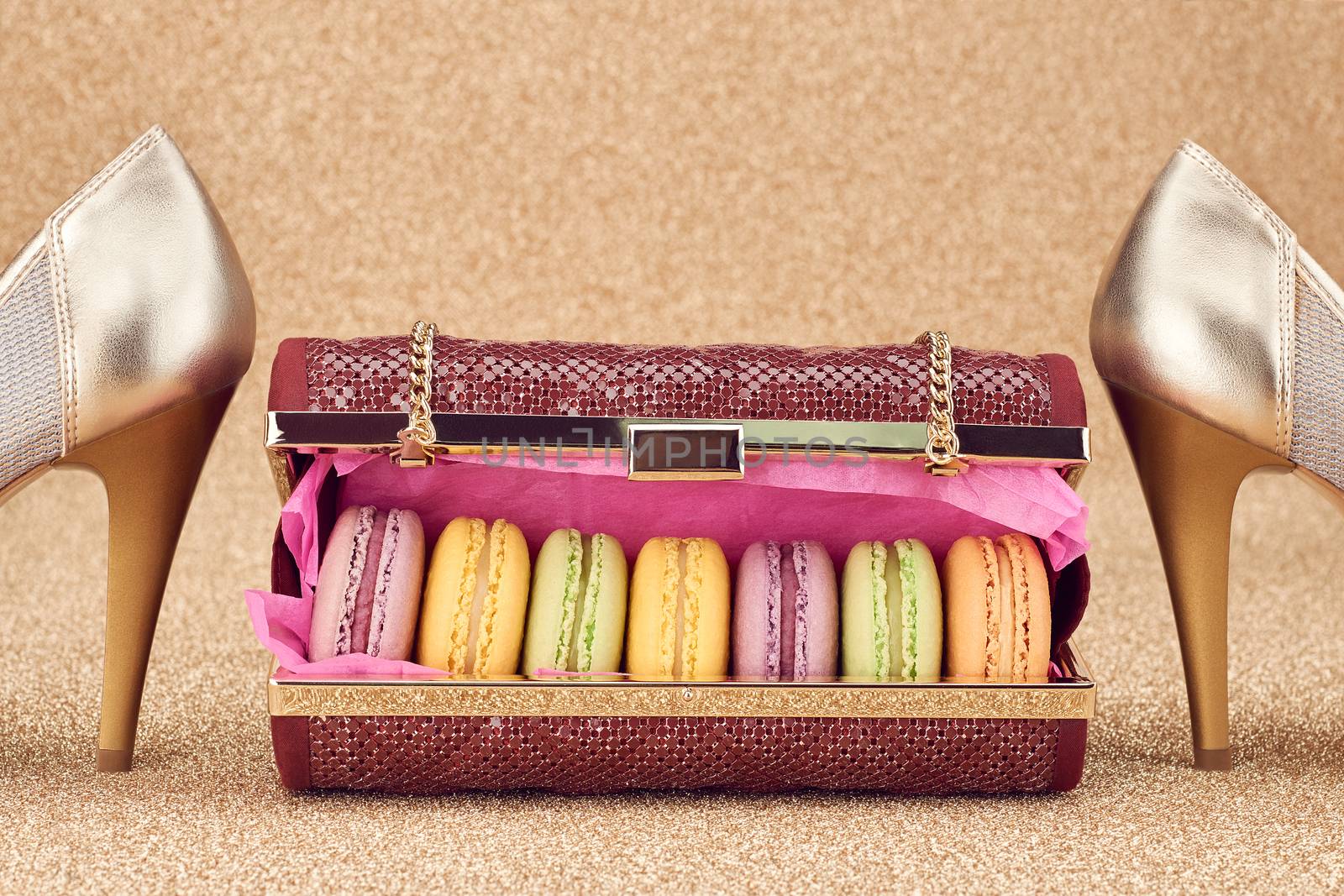 Macarons french in handbag, shoes high heels.Luxury shiny glamor fashion clutch. Colorful dessert. Unusual creative art, gold party background, bokeh, closeup. Still life, vintage