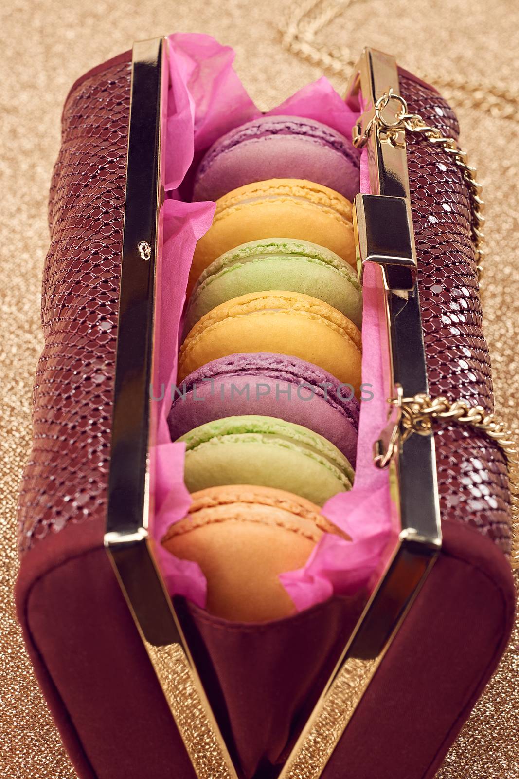 Macarons french in handbag. Luxury shiny glamor fashion clutch. Sweet colorful dessert. Unusual creative art, gold party background, bokeh, closeup. Vintage